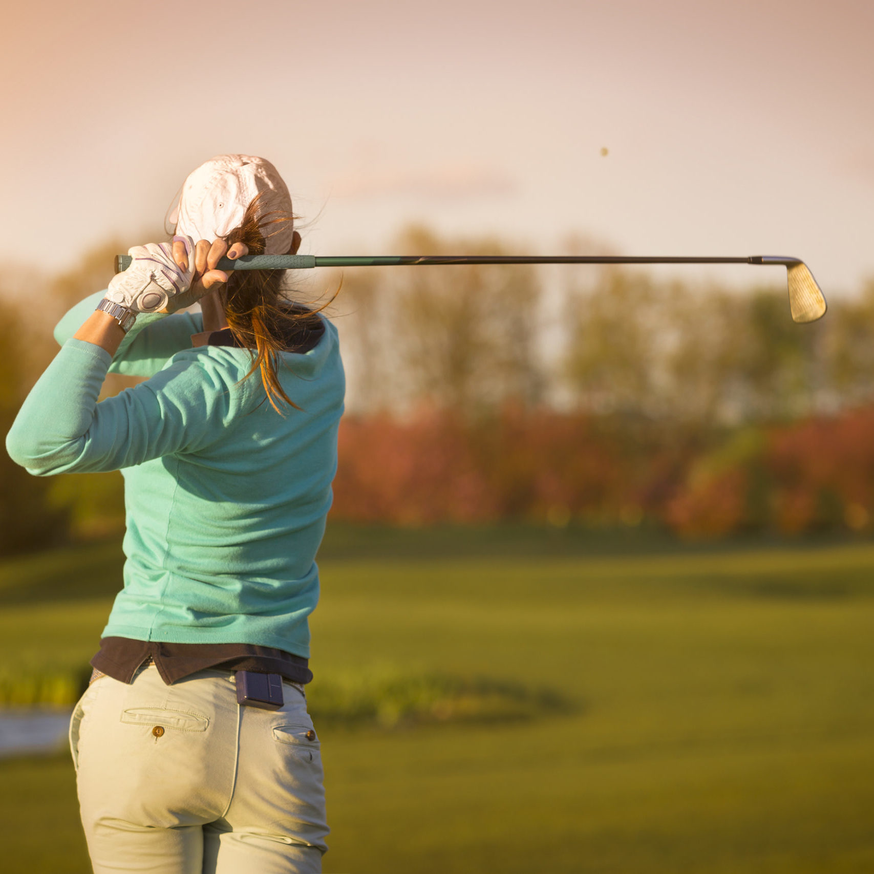 Close up of female golf player swinging golf club on fairway during sunset.